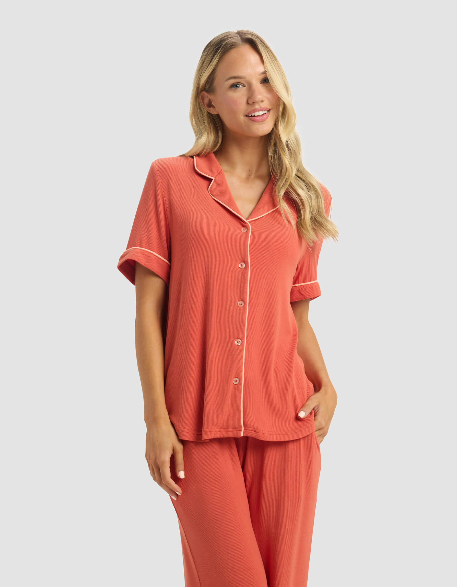 A woman with long blonde hair smiles with one hand in her pocket, wearing the Cozy Earth Women's Bamboo Rib-Knit Classic Short Sleeve Pajama Top and matching pants against a light gray background.