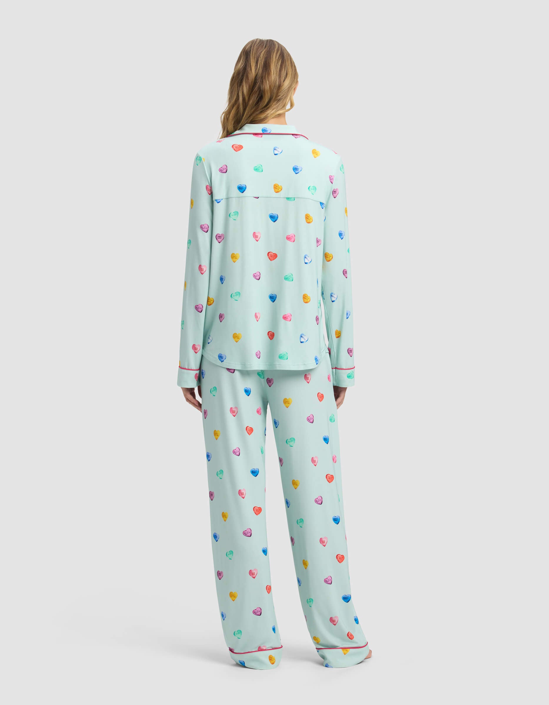 A person with long hair wears the Cozy Earth Women's Bamboo Stretch-Knit Long Sleeve Pajama Set in light blue with multicolored hearts, shown from the back against a plain light gray background.|Color:Seafoam Sleepy Hearts