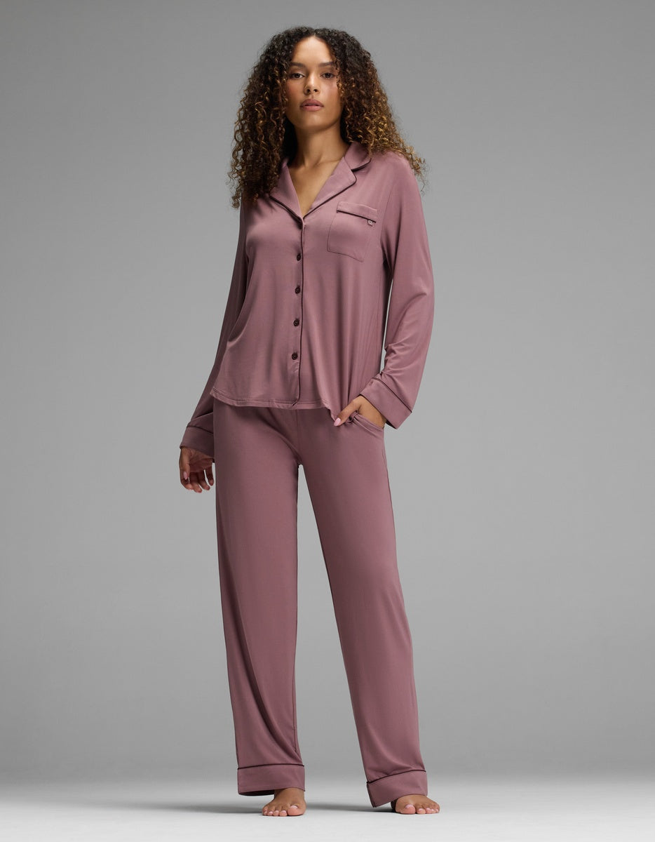 A woman wears a mauve Cozy Earth Women’s Bamboo Stretch-Knit Long Sleeve Pajama Set, featuring a button-down collar top and matching straight-leg trousers.