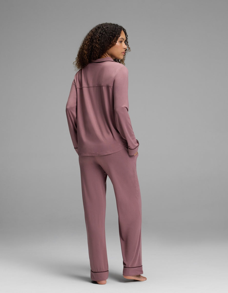 A person wearing a dusty pink Women’s Bamboo Stretch-Knit Long Sleeve Pajama Set with black piping trim.