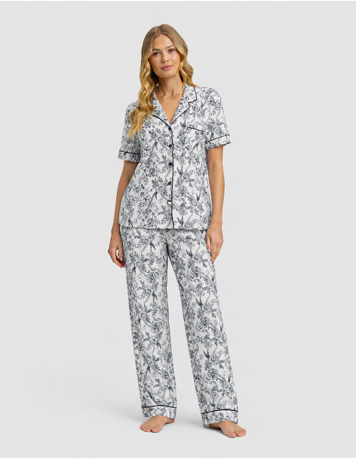 A woman with long, wavy blonde hair models the Cozy Earth Women's Bamboo Stretch-Knit Short Sleeve & Pant Pajama Set in a black and white floral print.