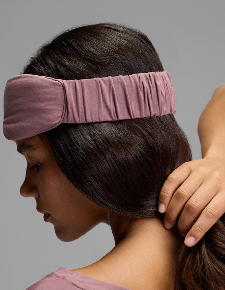 A person wearing a dusty pink Bamboo Stretch-Knit Sleep Mask with a wide, ruched elastic band.