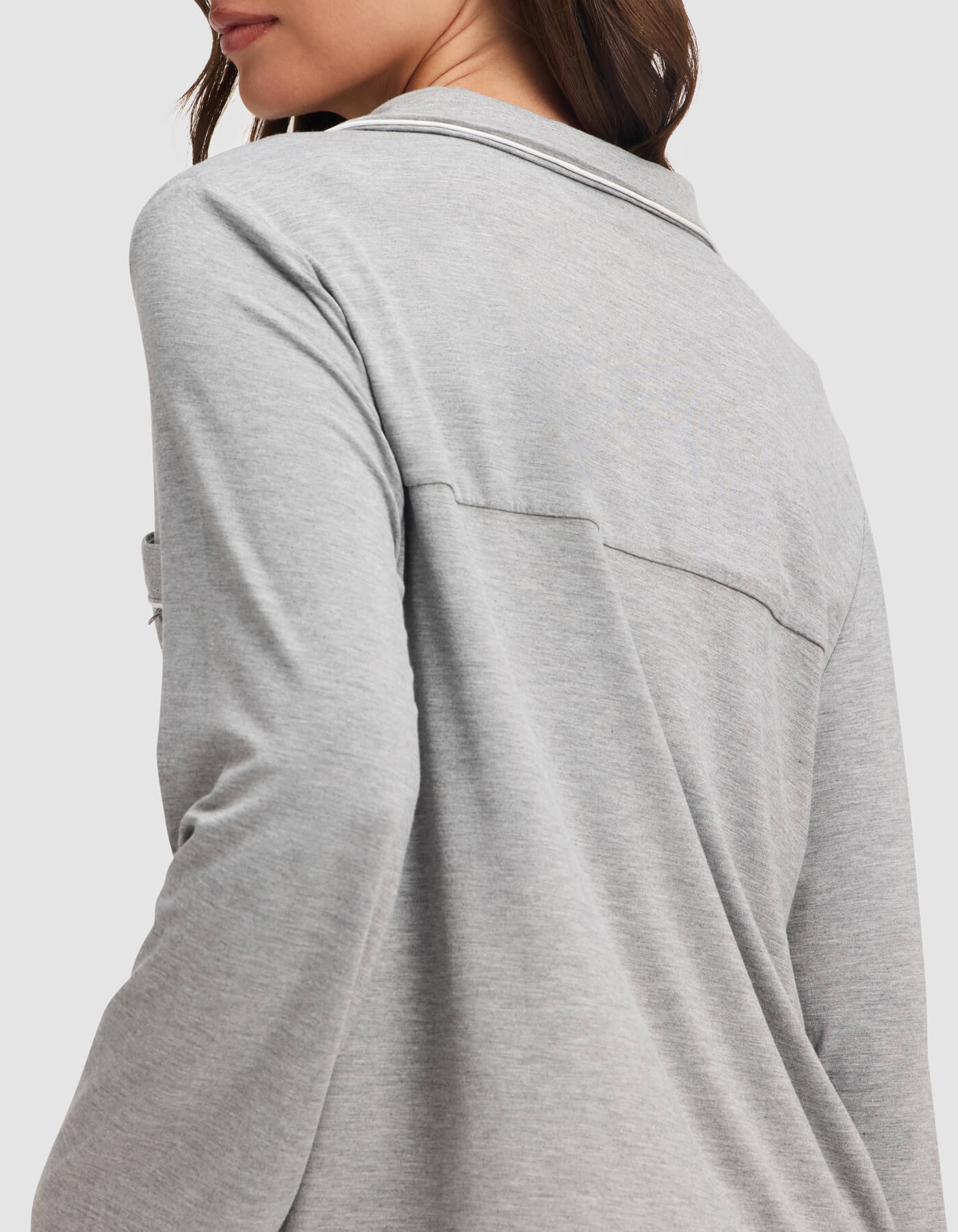 A woman is shown from the back and side wearing the Cozy Earth Women's Bamboo Stretch-Knit Long Sleeve Pajama Top in light gray, highlighting its relaxed fit and soft, stretchy fabric across the upper back and shoulders.