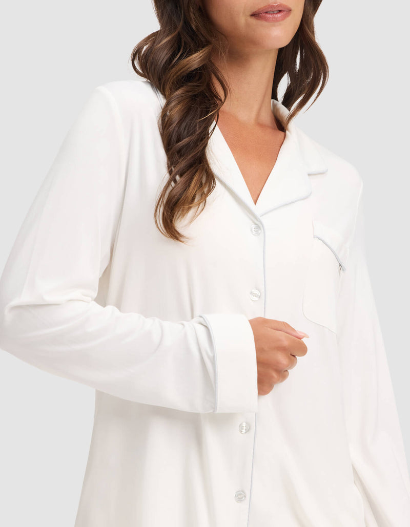 A woman with wavy brown hair models the Cozy Earth Women's Bamboo Stretch-Knit Long Sleeve Pajama Top, featuring a chest pocket, against a plain light background.