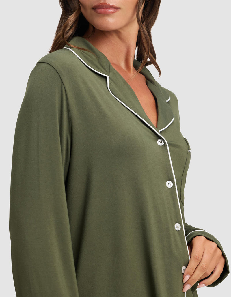 A woman models the Cozy Earth Women's Bamboo Stretch-Knit Long Sleeve Pajama Top in olive green with white piping along the collar and buttons, shown from shoulders to mid-torso against a plain background.