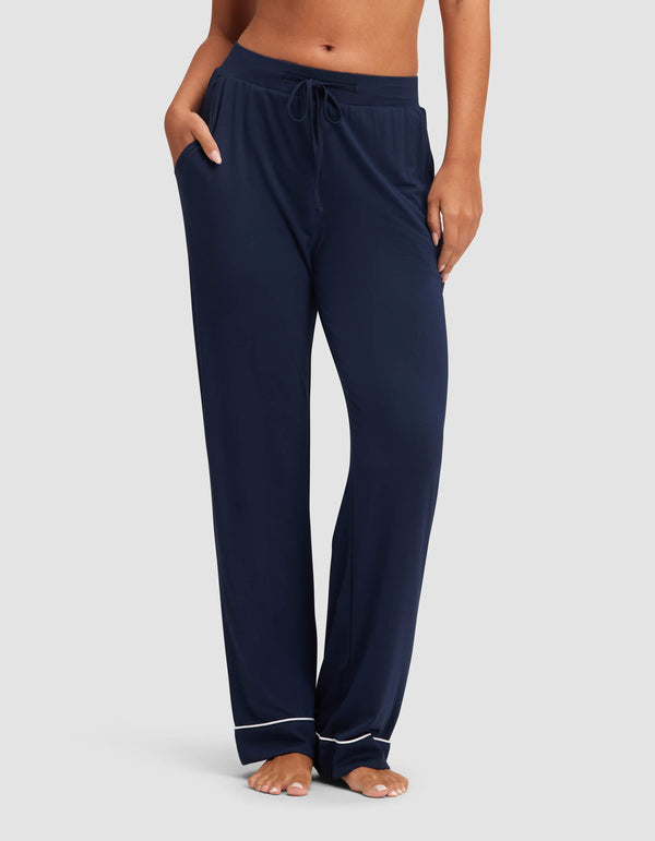 A woman stands barefoot against a plain background wearing Cozy Earth's Women's Bamboo Stretch-Knit Pajama Pant, featuring a loose fit, drawstring waist, and white piping near the hems.|Color:Navy
