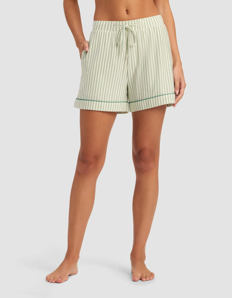 A person stands barefoot wearing Cozy Earth's Women's Bamboo Stretch-Knit Pajama Short in light green and white vertical stripes with a drawstring waist and pockets, shown from mid-torso to feet against a plain background.