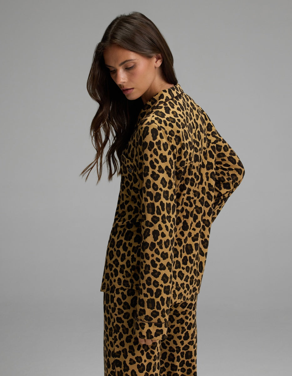 A person with long brown hair is wearing the Cozy Earth Women’s Bamboo Stretch-Knit Long Sleeve Pajama Top in a matching set. They are facing sideways and looking down, set against a plain gray background.