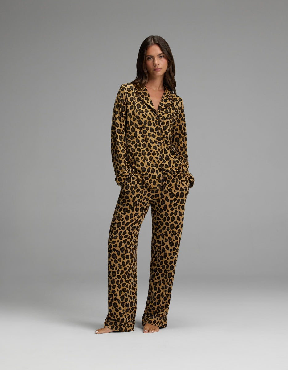 A woman stands barefoot against a plain grey background, wearing the Cozy Earth Women’s Bamboo Stretch-Knit Long Sleeve Pajama Set featuring a matching brown and black leopard print.|Color:Leopard Print in Onyx