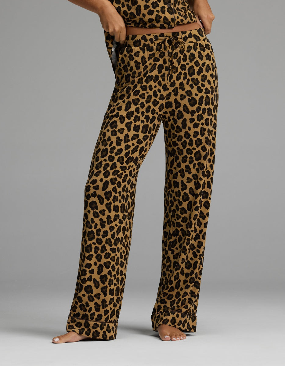 A person stands barefoot wearing Cozy Earth’s Women’s Bamboo Stretch-Knit Pajama Pant in a loose-fitting silhouette, featuring a brown base with a black leopard print. The image is cropped at the torso, concealing the individual’s upper body and face.|Color:Leopard Print in Onyx