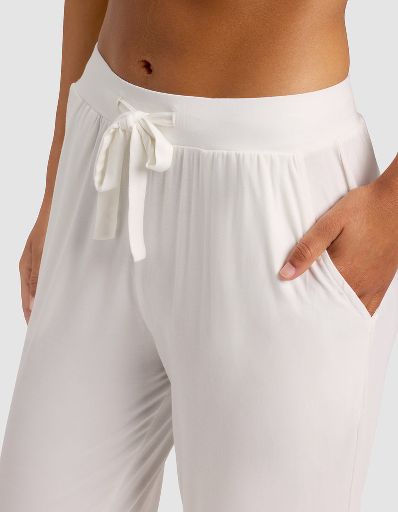 A woman wears Cozy Earth's Women's Bamboo Stretch-Knit Pant in white, shown from waist to mid-thigh with a hand in one pocket against a plain background.