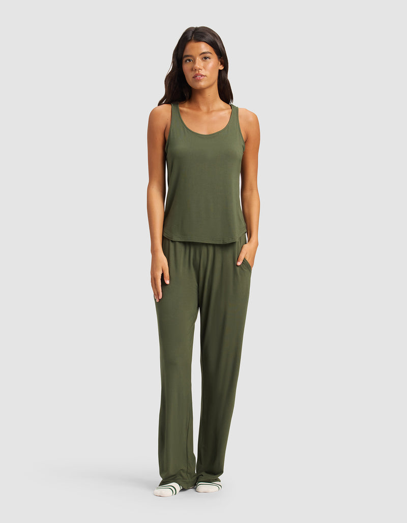 A woman faces forward wearing Cozy Earth’s Women's Bamboo Stretch-Knit Pant in olive green with a matching sleeveless tank top and white slide sandals, standing against a plain light gray background.