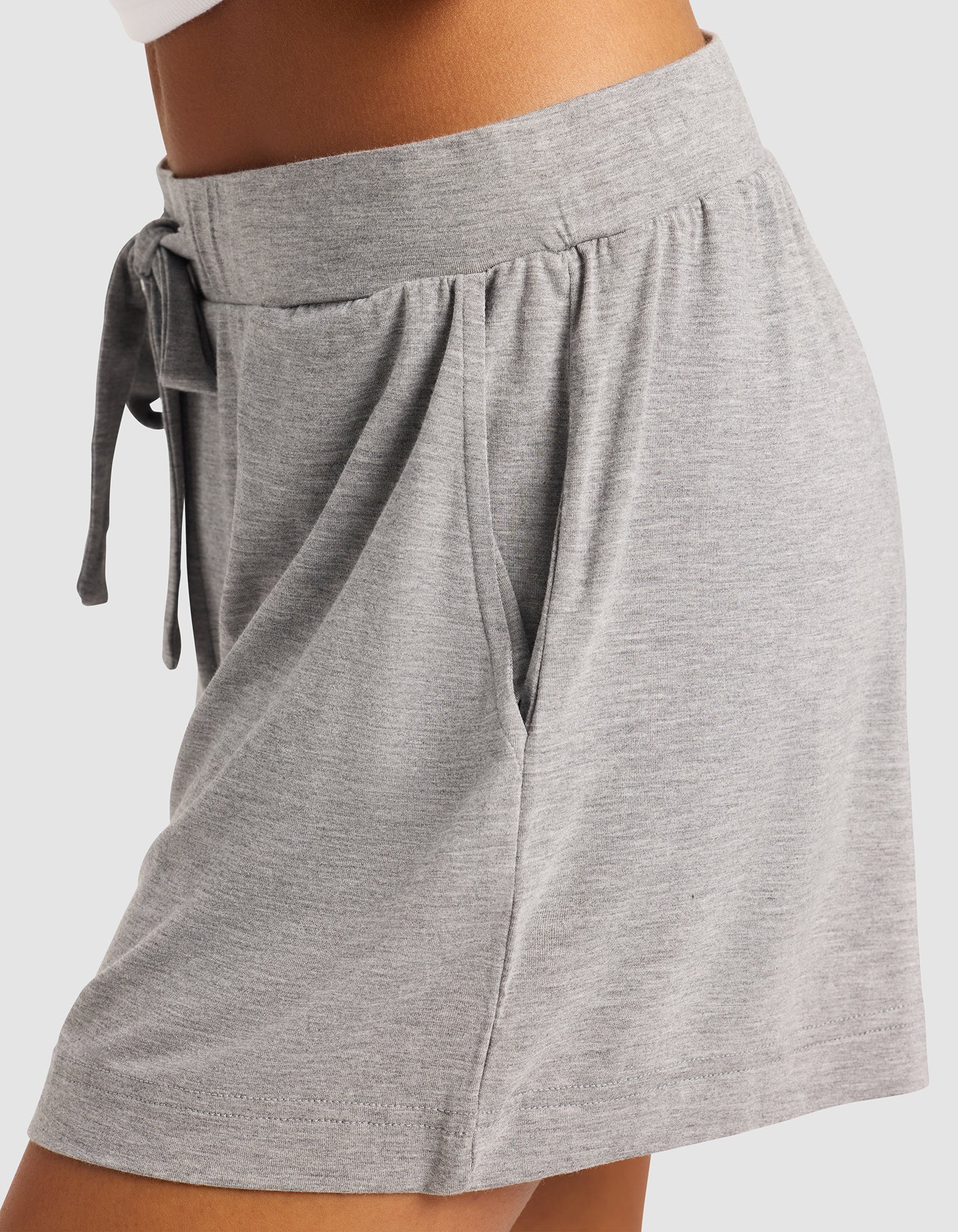 A close-up side view of a person wearing Cozy Earth Women's Bamboo Stretch-Knit Shorts in light gray, featuring a soft knit fabric, elastic waistband with drawstring, and side pocket for a comfortable, casual look.|Color:Heather Grey