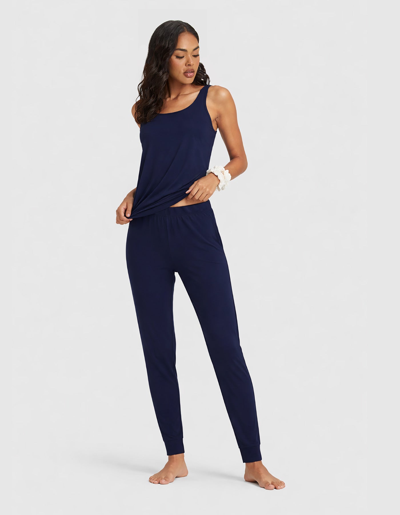 A woman poses barefoot in the Cozy Earth Women's Bamboo Stretch-Knit Tank & Tapered Pant Set, featuring a navy blue sleeveless top and matching jogger pants, against a plain light gray background.|Color:Navy