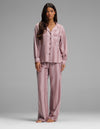 A woman stands barefoot, facing forward against a plain gray background, wearing the Cozy Earth Women’s Belmont Long Sleeve Pajama Set in Viola Stripe. The loose-fitting, button-up pajamas feature long sleeves and matching pants with a vertical stripe pattern.|Color:Viola Stripe