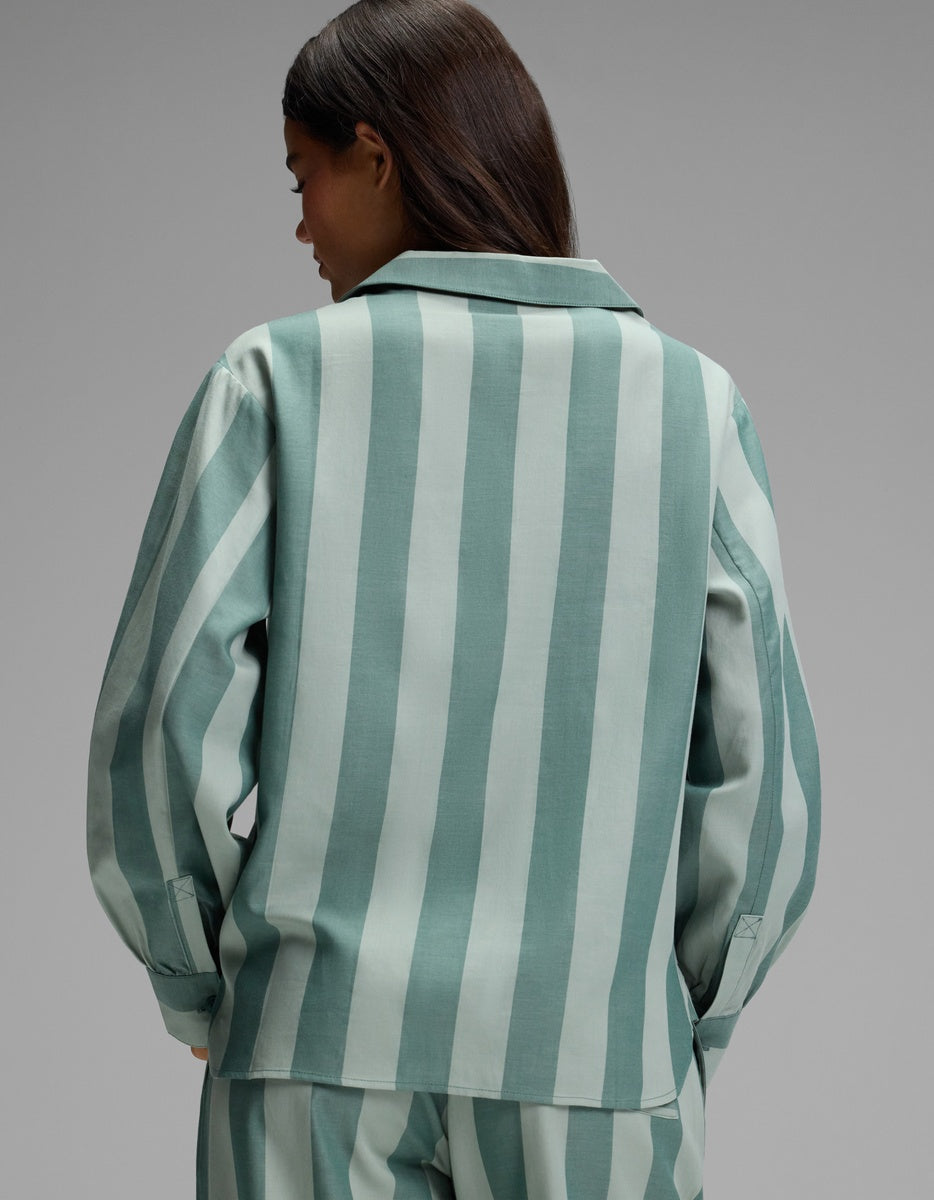 A person with long dark hair is shown from the back, wearing the Cozy Earth Women’s Belmont Long Sleeve Pajama Top in a light green and white vertical stripe pattern, set against a plain gray background.