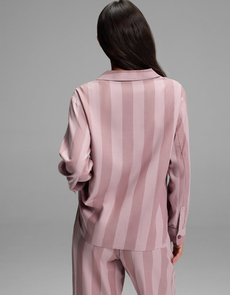 A woman with long dark hair is shown from the back, wearing the Cozy Earth Women’s Belmont Long Sleeve Pajama Top in a matching pink striped set, standing against a plain gray background.