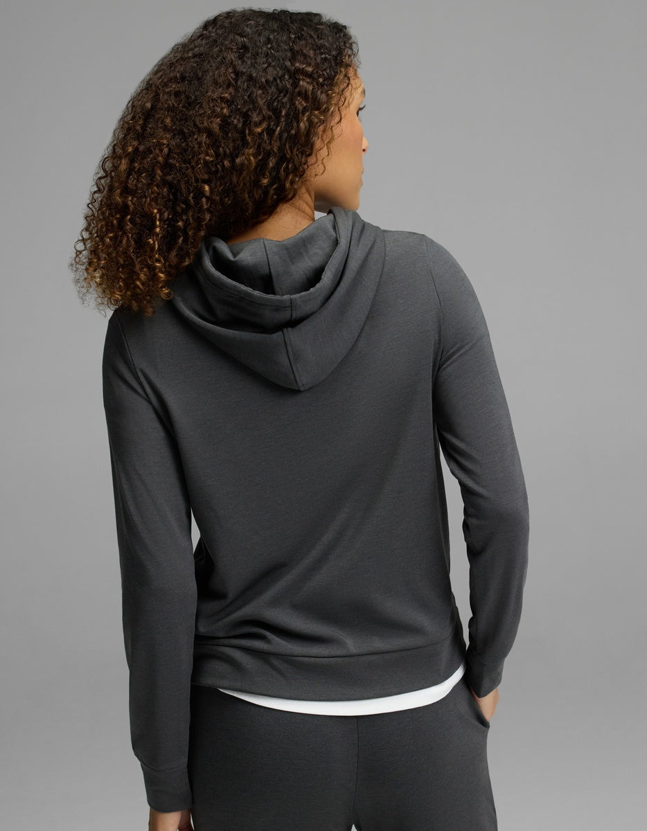 A woman with curly hair is shown from the back, wearing the Cozy Earth Women’s Brushed Bamboo Hoodie in dark gray, against a plain gray background.