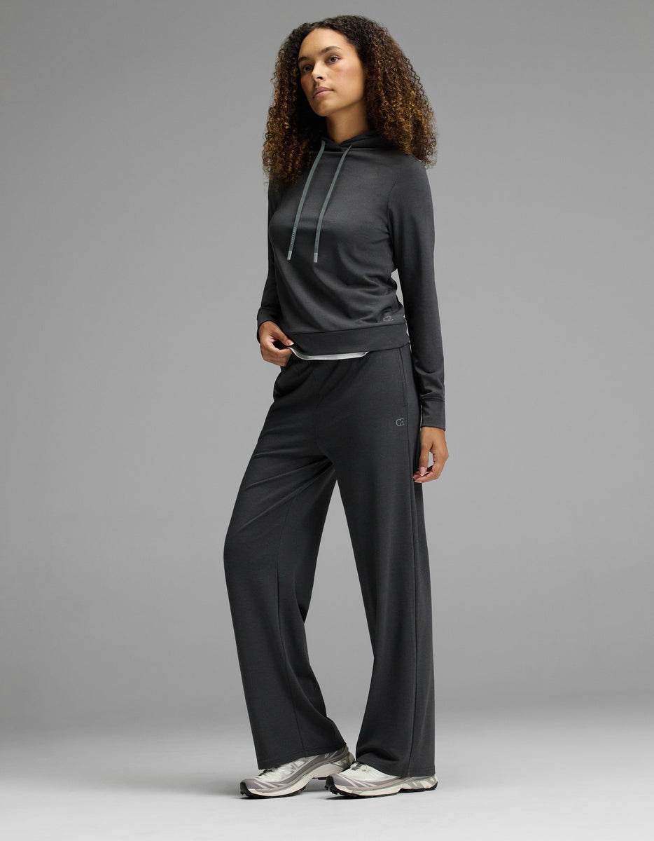 A person stands posing in a Cozy Earth Women’s Brushed Bamboo Hoodie, styled with matching wide-leg pants and silver athletic shoes, against a plain gray background.