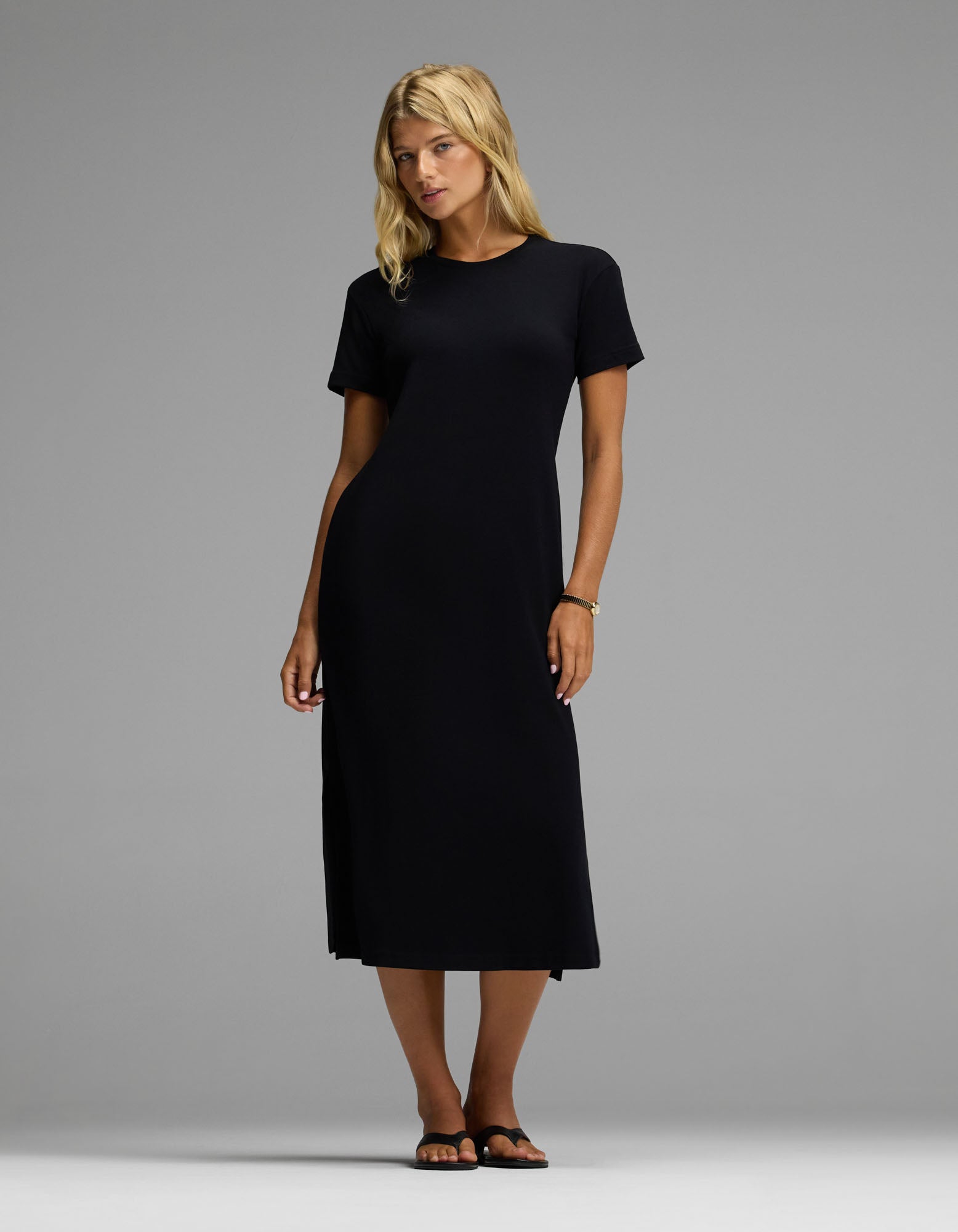 A woman wearing the Cozy Earth Women’s Brushed Bamboo Midi Dress in black, paired with black sandals, stands against a plain grey background.