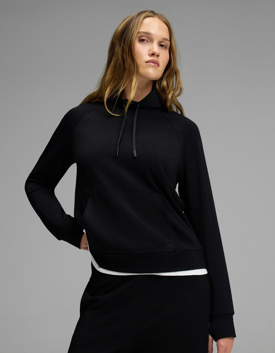 A person with long, wavy hair stands confidently against a plain gray background wearing Cozy Earth’s Women’s Brushed Bamboo Mock Neck in black and matching black pants.|Color:Black