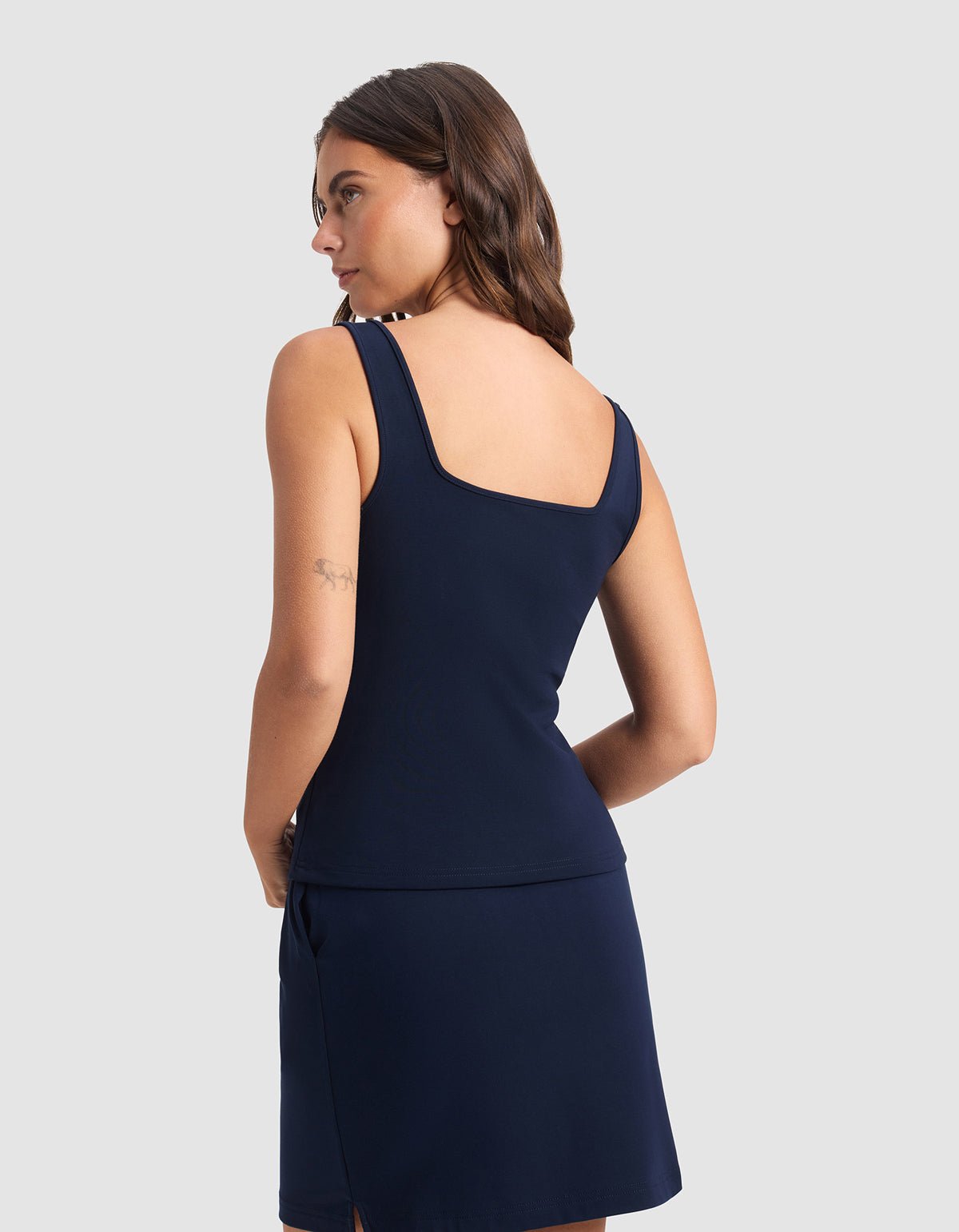 A woman with long brown hair wears the Cozy Earth Women's Brushed Bamboo Square Neck Tank in navy blue, facing slightly away to highlight its square neckline and shoulder straps, set against a plain light gray background.|Color:Navy