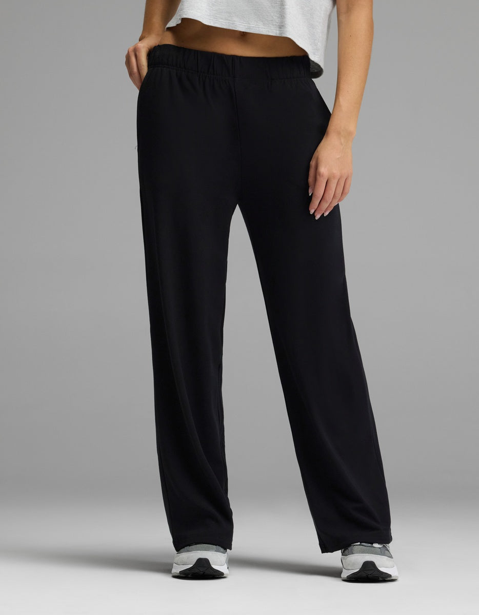 A person stands against a gray background—only the lower body is visible—wearing Cozy Earth’s Women’s Brushed Bamboo Wide Leg Pull-On Pant in black, paired with a white cropped top and white sneakers.|Color:Black