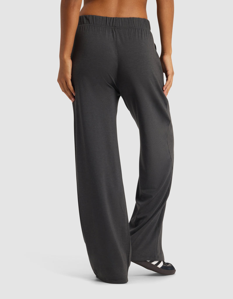 A woman is shown from the back wearing Cozy Earth's Women's Brushed Bamboo Wide Leg Pull-On Pant in dark gray with black sandals, posed against a plain white background.