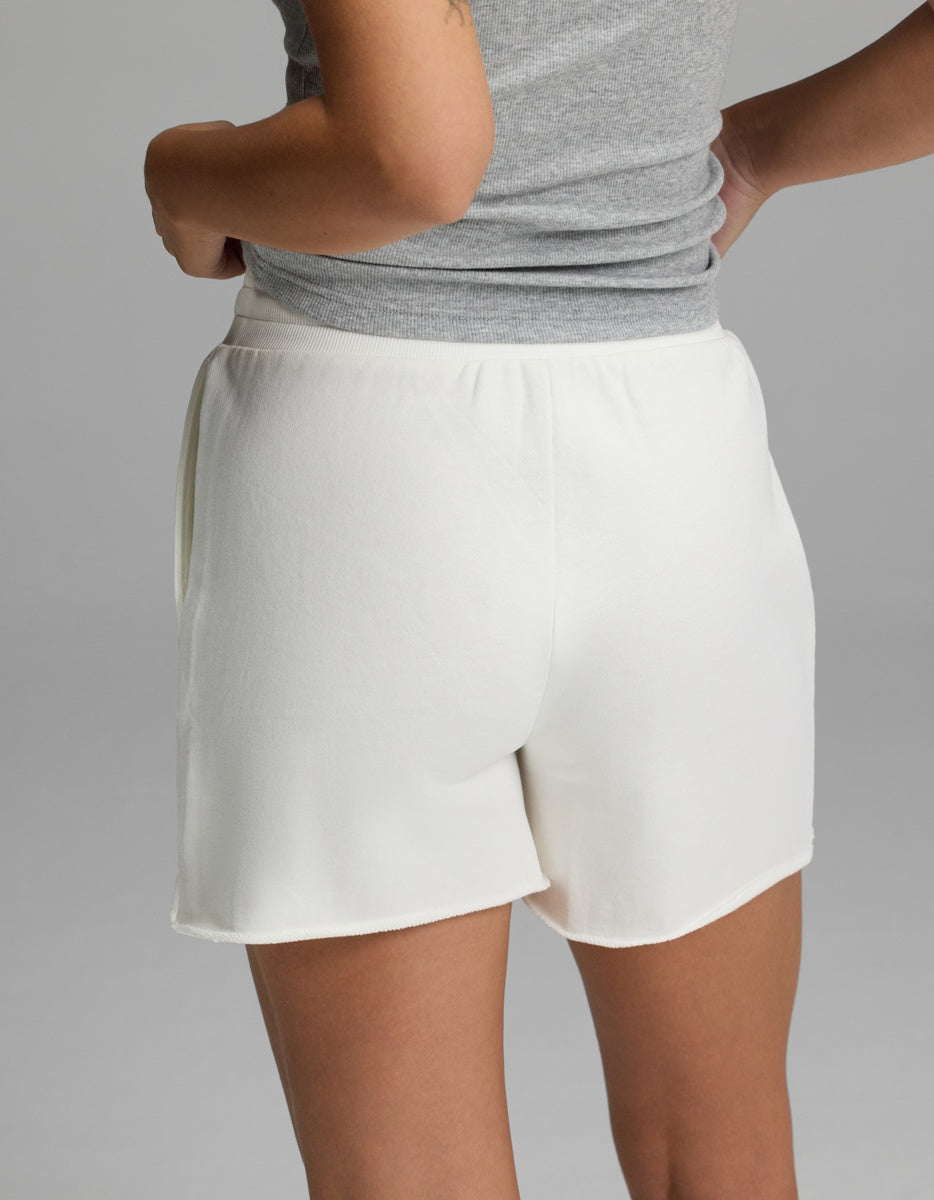 A person, seen from behind with hands on hips, is wearing Cozy Earth’s Women’s Chelsea Short in white and a gray sleeveless top against a plain light gray background.