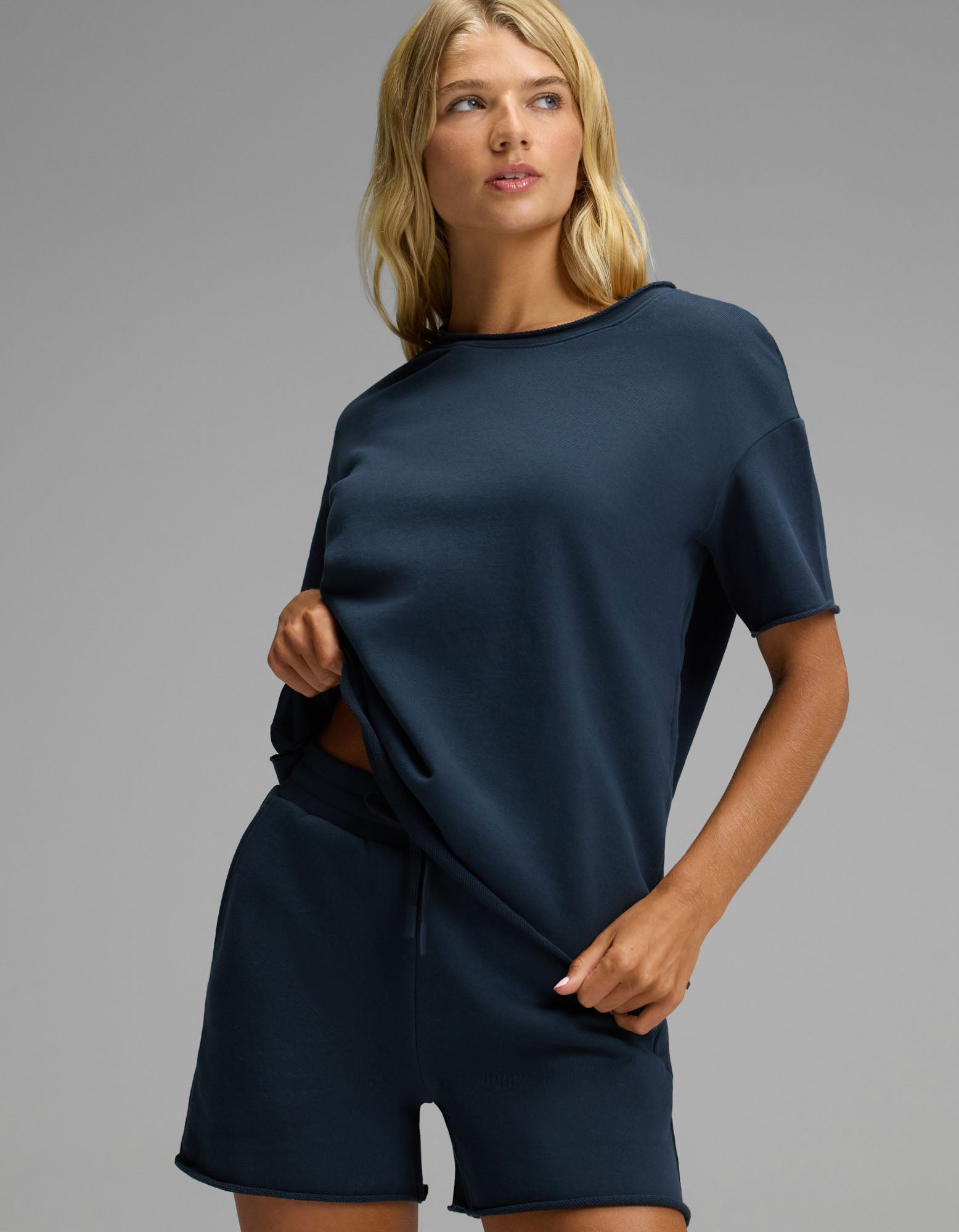 A woman stands against a plain background wearing the Cozy Earth Women’s Chelsea Short Sleeve Set in navy blue. She holds the side of her shirt and looks slightly to her left.