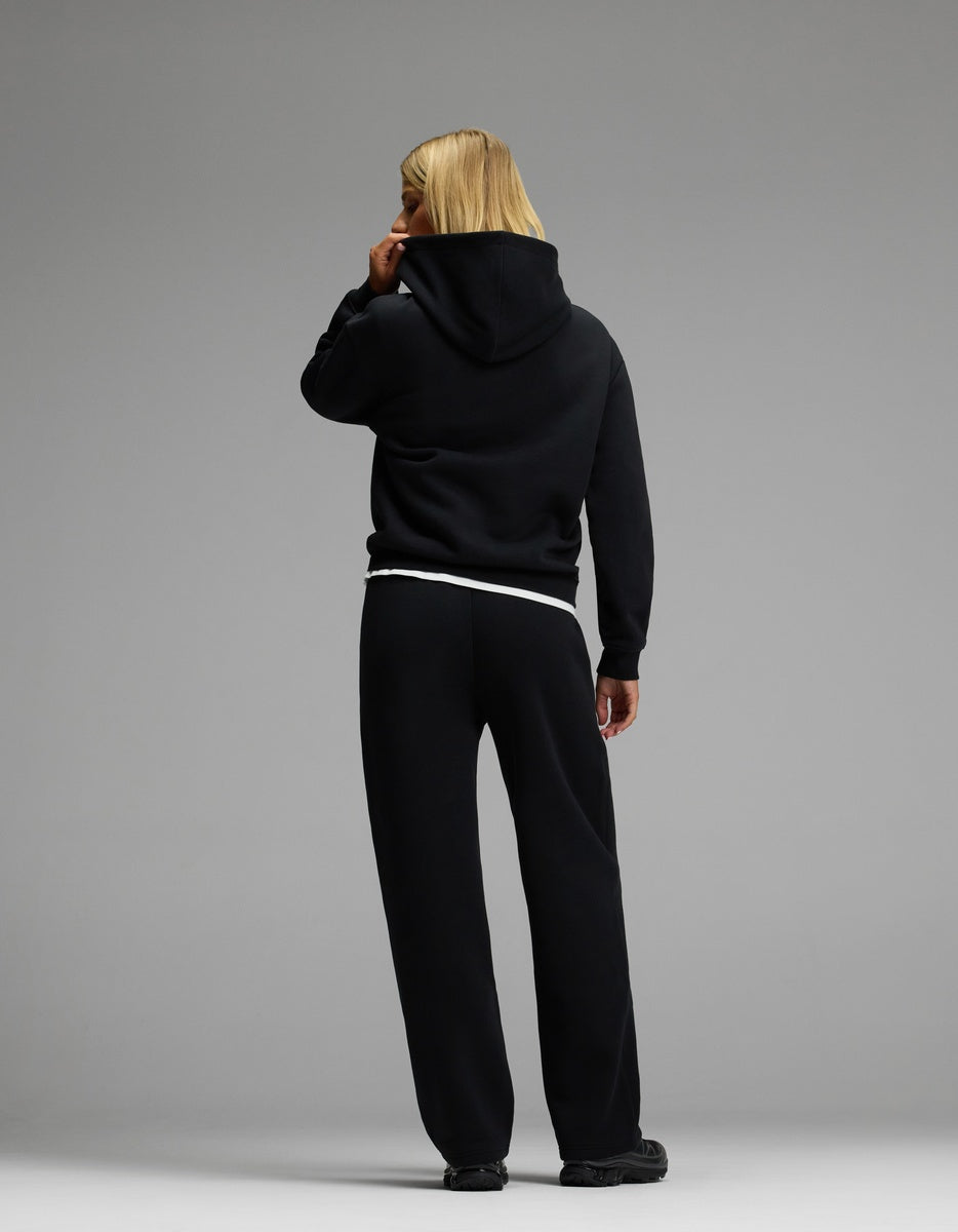 A person with blonde hair models the Women’s CityScape Hoodie & Wide Leg Pant Set from Cozy Earth in black, standing with their back to a plain gray background.
