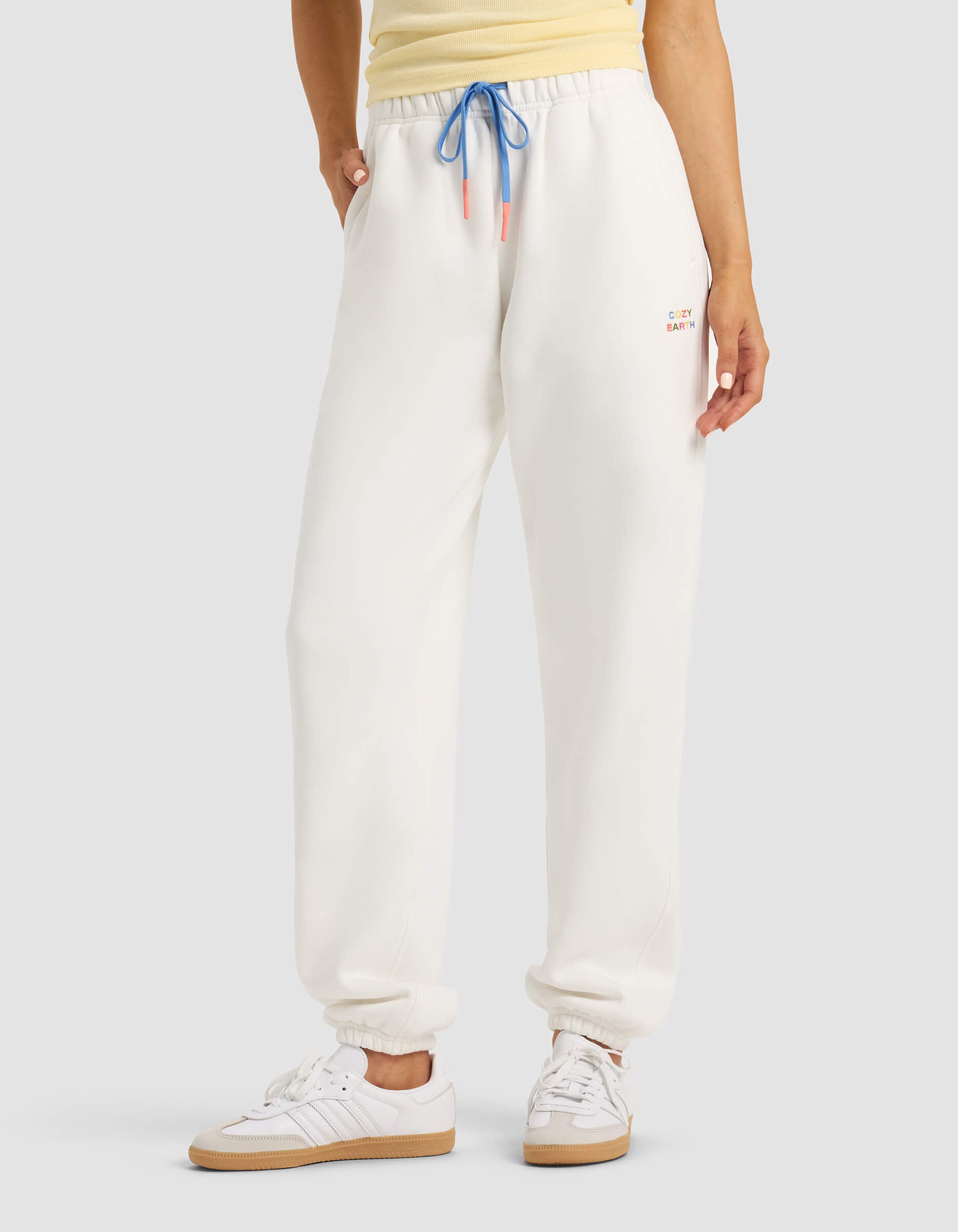 A person models Cozy Earth's Women's Cityscape 2.0 Sweatpant in white, paired with a yellow top and white sneakers, hands in pockets, against a plain background. |Color:Sea Salt