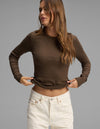 A woman with long brown hair wears the Cozy Earth Women's Fine Ribbed Long Sleeve Tee in brown, paired with high-waisted white jeans, standing against a plain gray background.|Color:Espresso