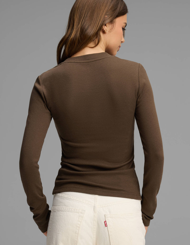 A woman with brown hair, wearing the Cozy Earth Women's Fine Ribbed Long Sleeve Tee in brown and white jeans, is standing with her back to the camera against a plain gray background.