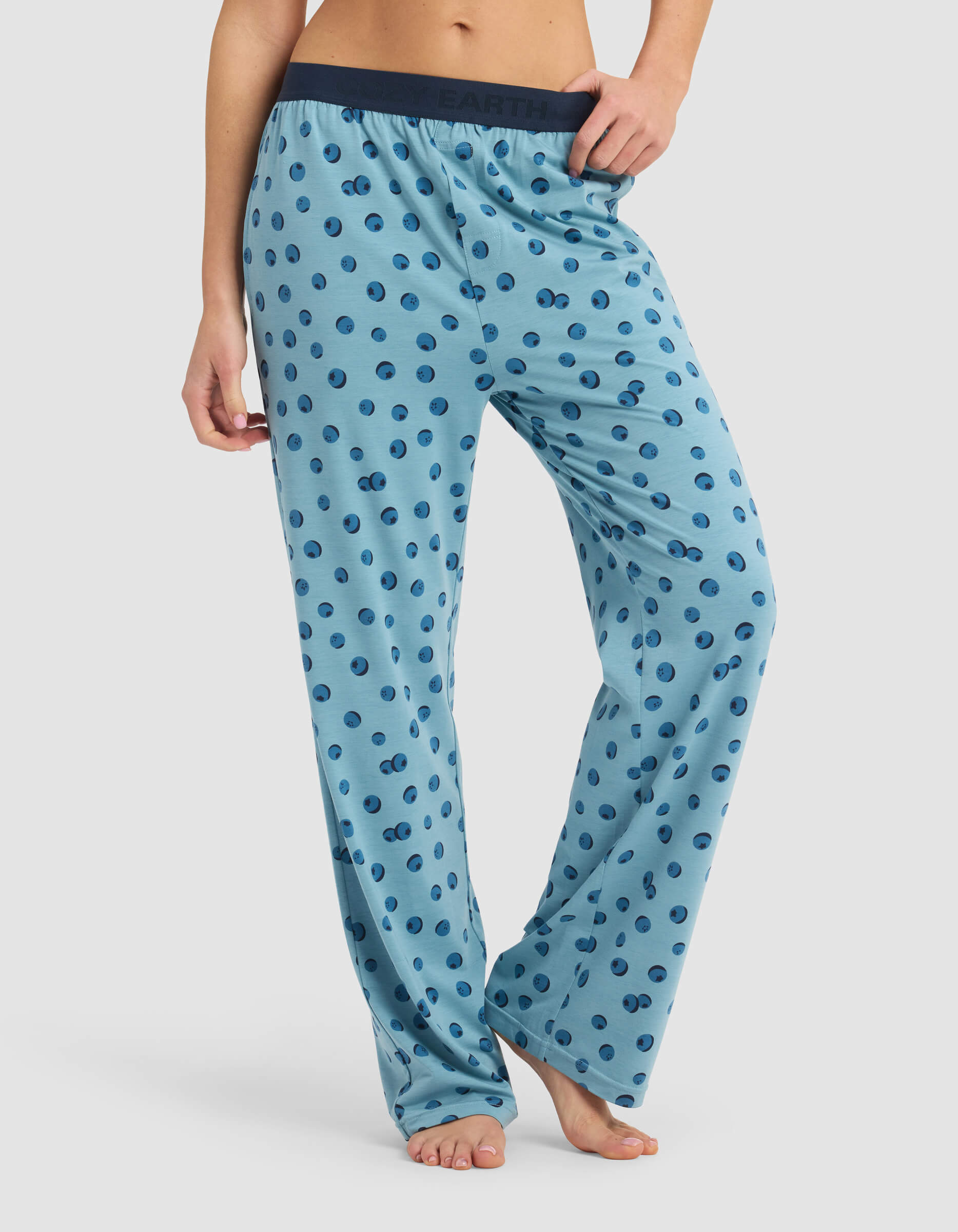 Model is wearing Cozy Earth's Women's First Layer Pajama Pant in light blue with dark blue polka dots and a dark elastic waistband, shown barefoot on a white background.|Color:Blueberries
