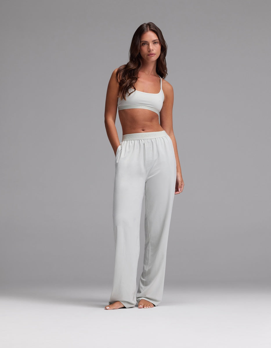 A woman with long brown hair stands barefoot against a plain gray background, wearing the Cozy Earth Women’s First Layer Pajama Soft Bra & Pajama Pant Set in Laurel.|Color:Laurel