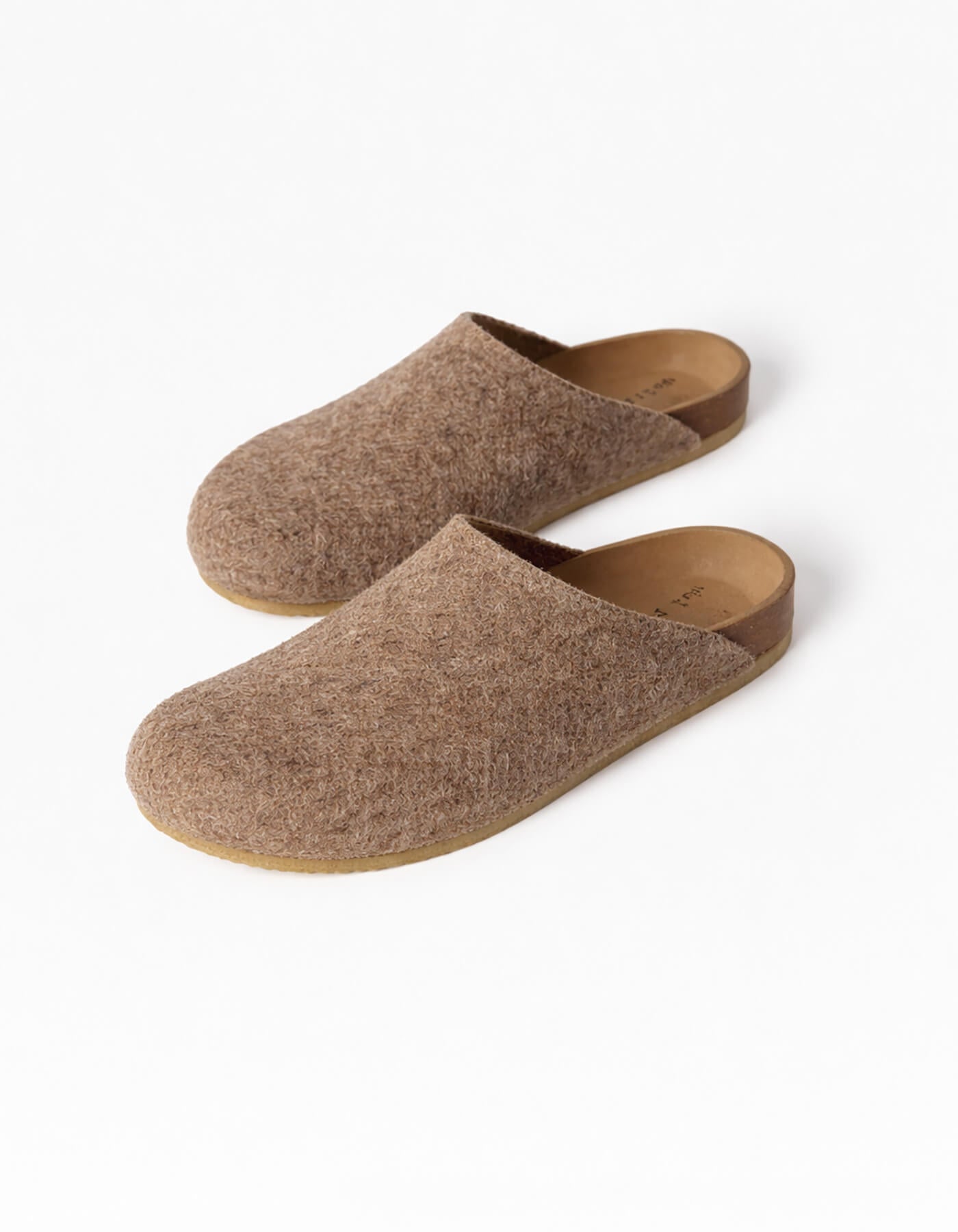 The Lakehouse Clog by Cozy Earth are brown woolen slip-on slippers with a cork sole, viewed from above. They feature a minimalist design perfect for indoor use against a light grey background. 
