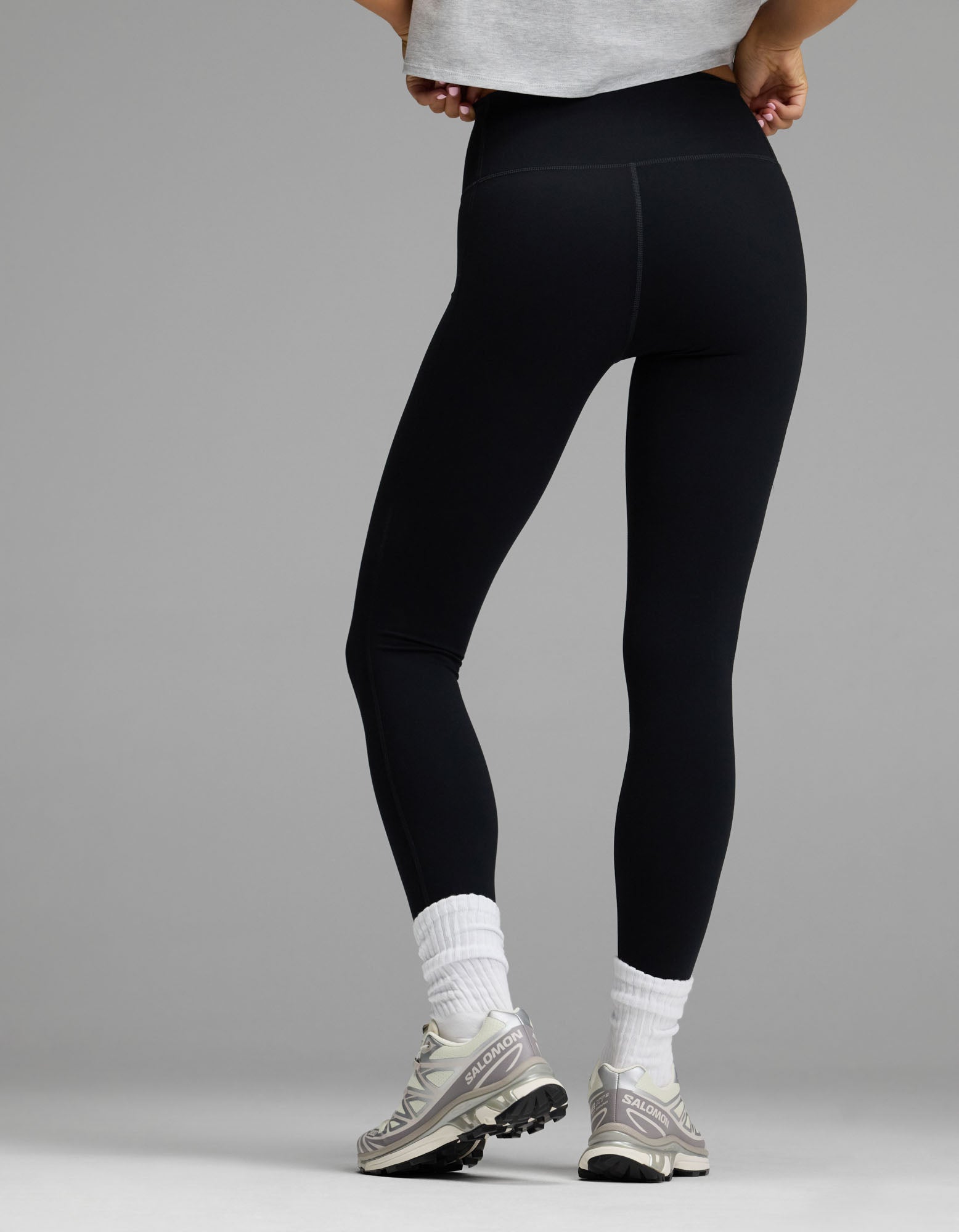 A person stands with their back to the camera wearing Cozy Earth’s Women’s Liv Legging, paired with white socks, gray sneakers, and a light gray cropped shirt, set against a plain gray background.