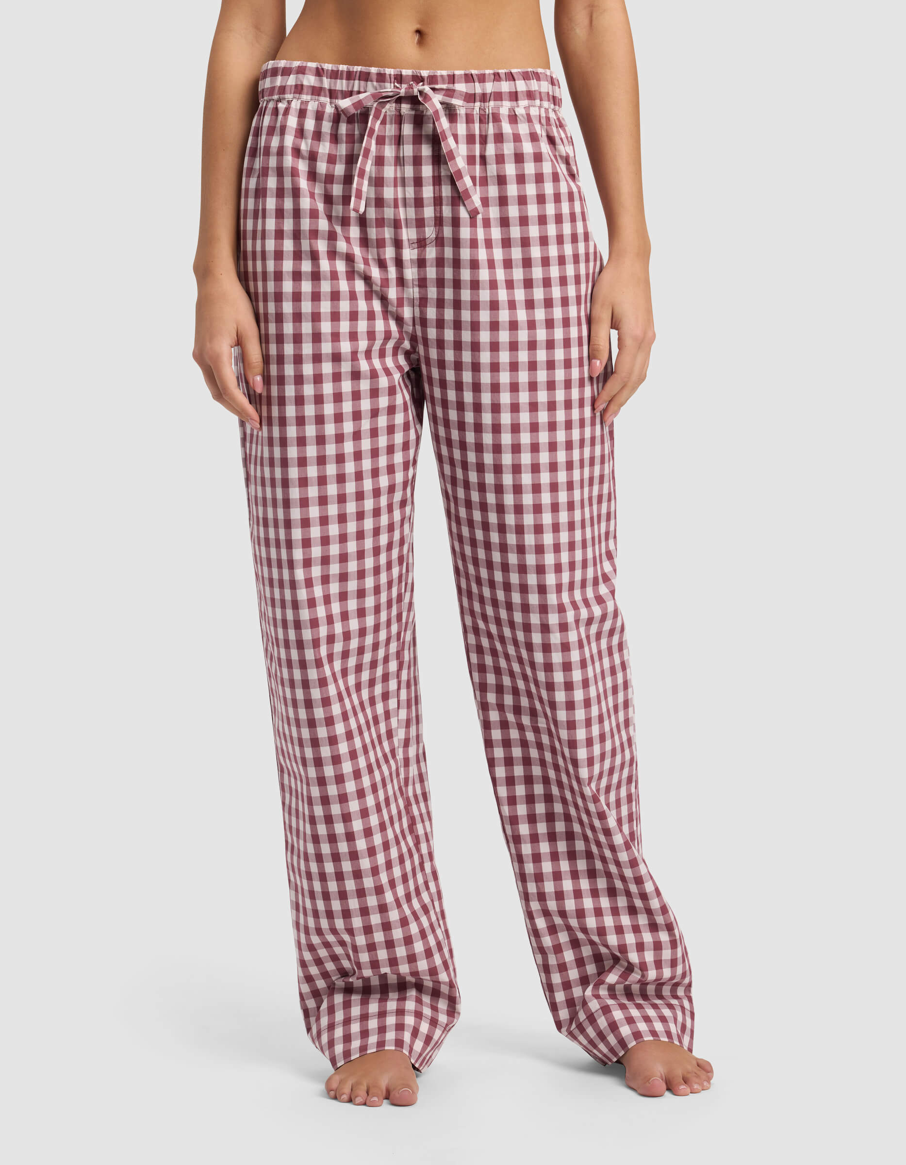 A woman stands barefoot wearing Cozy Earth Women's Sutton Pajama Pant, featuring a loose fit and red and white checkered pattern with a drawstring waistband, shown from shoulders down against a plain white background.