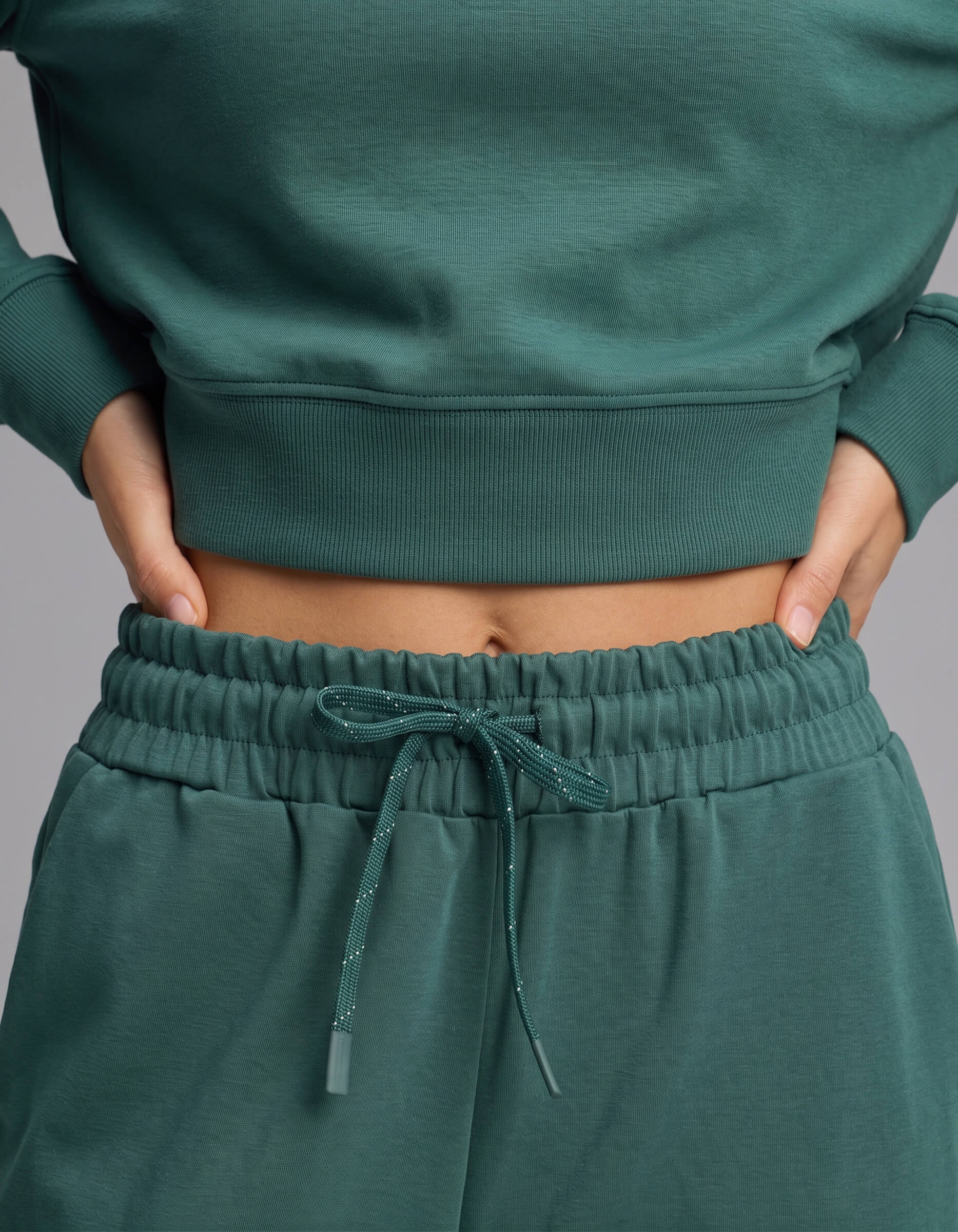 A person wearing the Cozy Earth Women's Versa Crewneck & Wide Leg Pant Set in green, with hands resting on their waist and midriff visible.