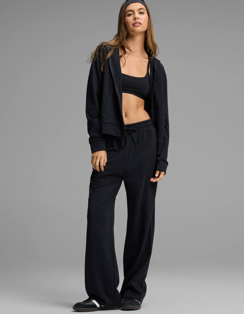 A woman stands against a plain gray background wearing the Cozy Earth Women's Versa Zip-Down Hoodie & Straight Leg Pant Set in black.
