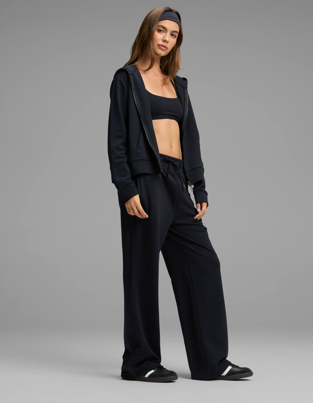 A woman stands confidently against a plain gray background, wearing the Cozy Earth Women's Versa Zip-Down Hoodie & Straight Leg Pant Set in black.|Color:Jet Black