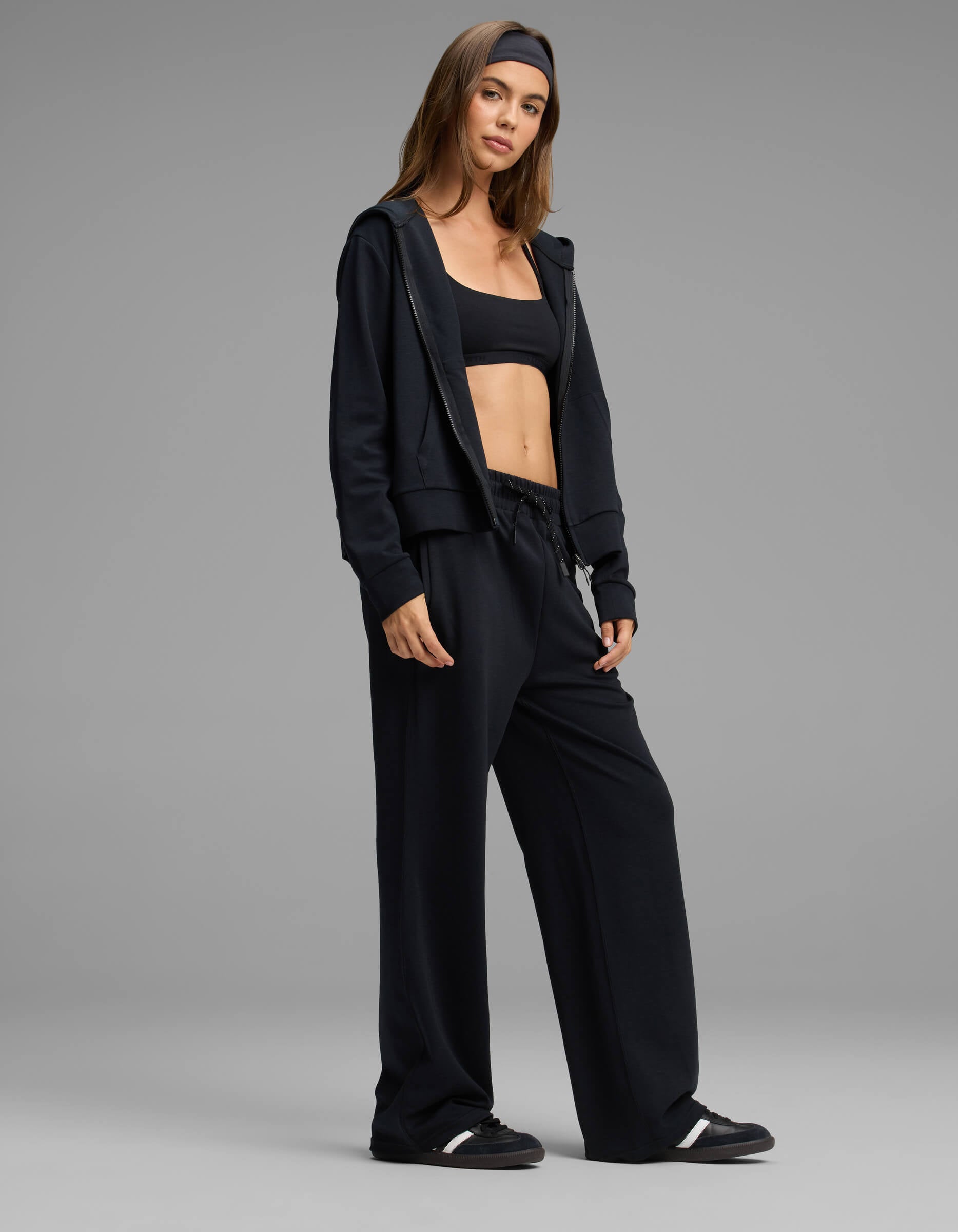 A woman stands confidently against a plain gray background, wearing the Cozy Earth Women's Versa Zip-Down Hoodie & Straight Leg Pant Set in black.