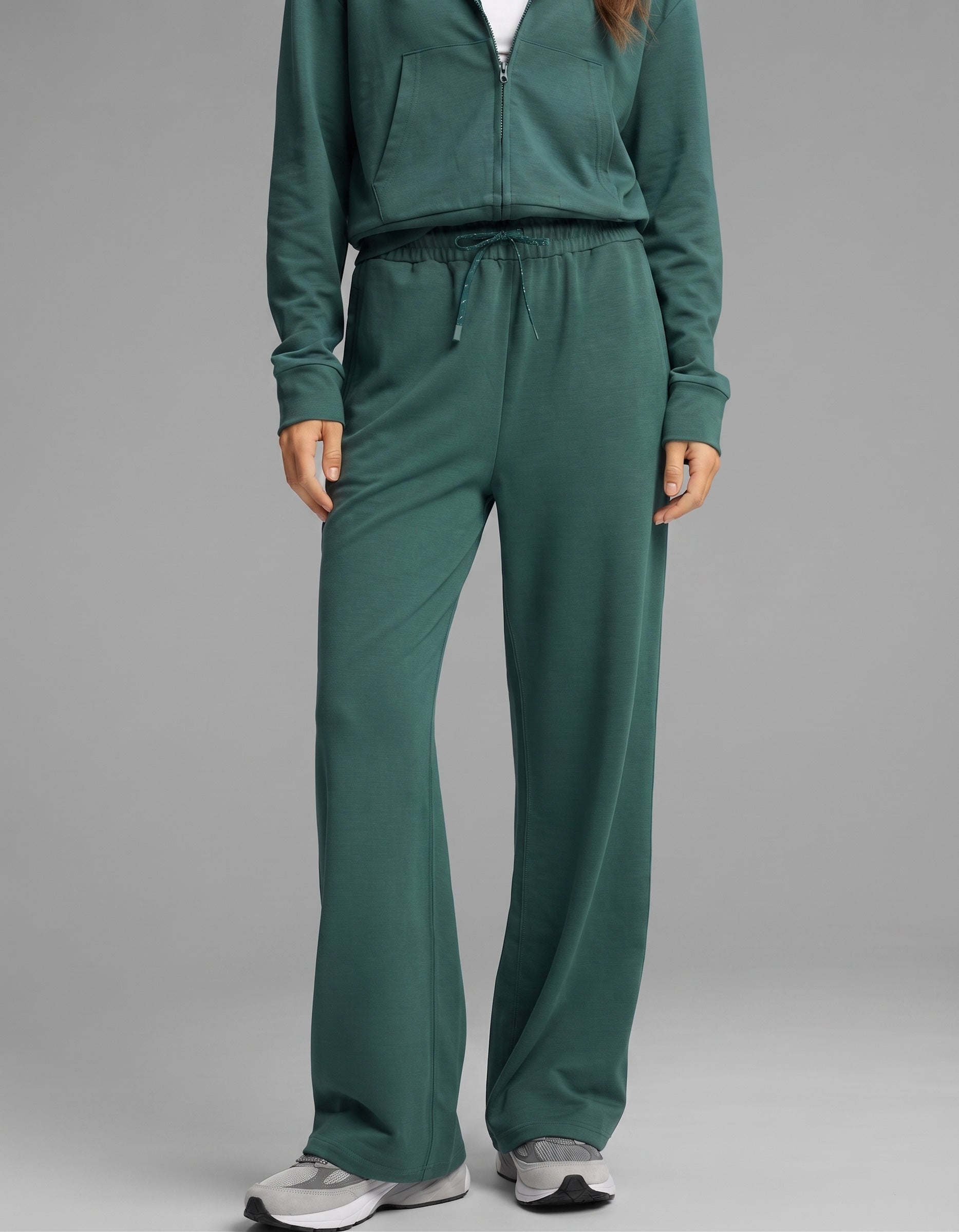 A person wearing the Cozy Earth Women's Versa Zip-Down Hoodie & Straight Leg Pant Set in green with gray sneakers, standing against a neutral background. The person’s face is not visible.
