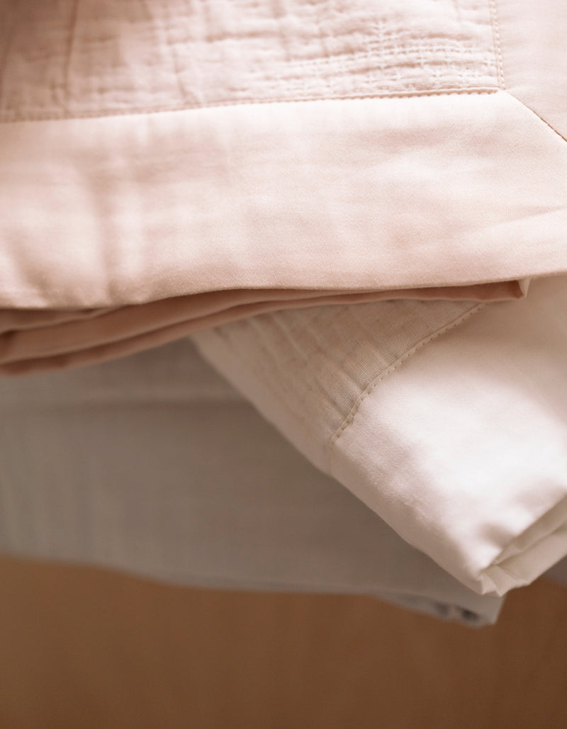 A close-up of the Cozy Earth Little Bee Matelasse Baby Blanket, featuring neatly folded layers of soft beige and white fabric that highlight its cozy texture and detailed edges.