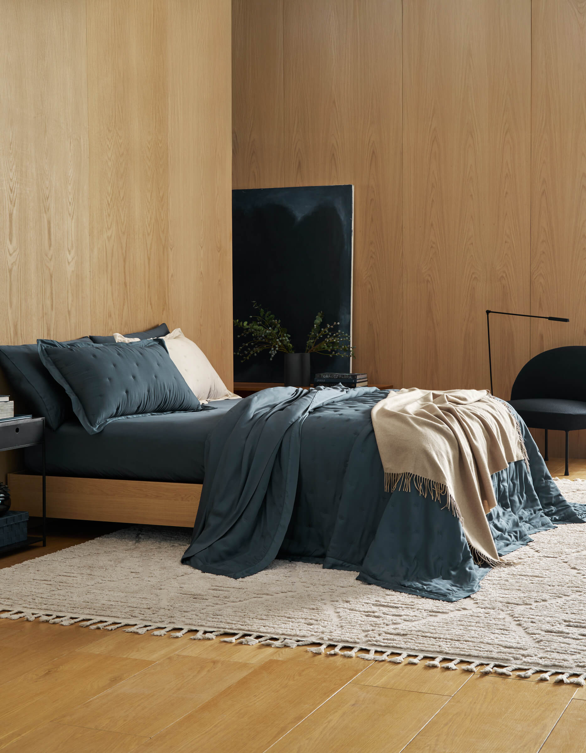 Modern bedroom with wooden walls, bed with blue bedding, and a painting.