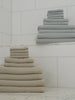 Harbor Mist and Sand colored waffle bath bundles rest on a marble floor in a shower room. Close ups of the towels can be seen