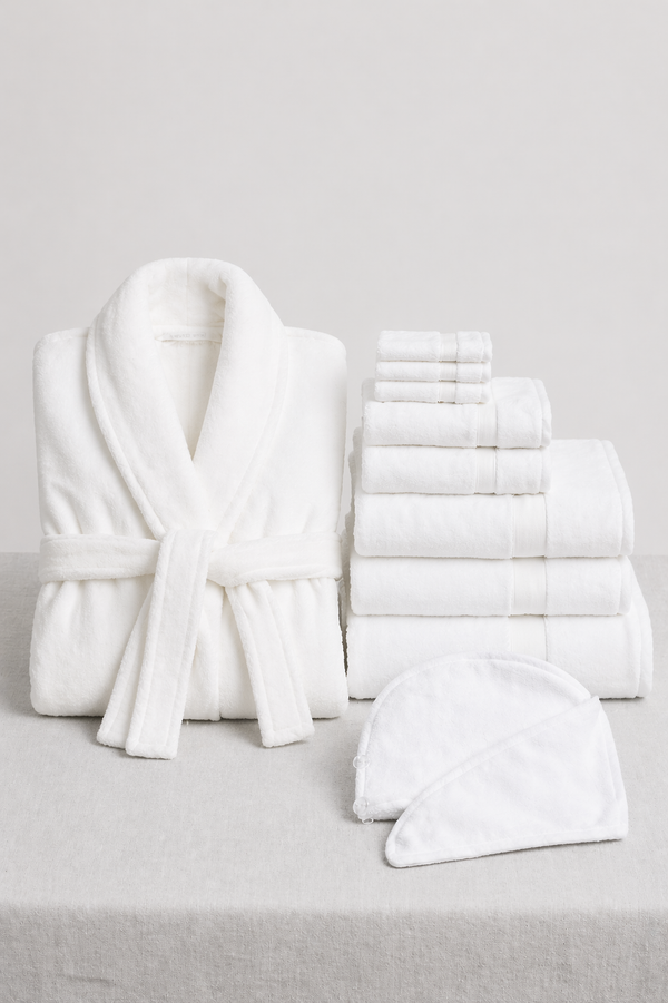The Cozy Earth Wrap Up Bundle, featuring a white bathrobe, assorted white towels, and a spa headband, is displayed on a light gray surface with a simple background.