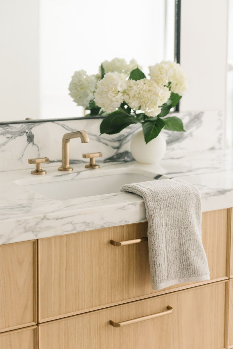 Ribbed Terry Hand Towels in the color Light Grey. Photo of product taken with the product draped over a white marble sink.