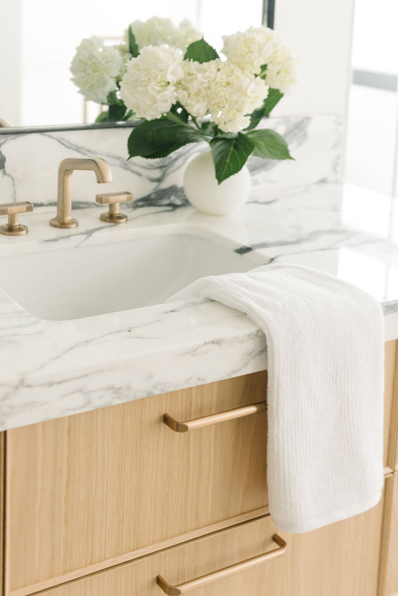 Ribbed Terry Hand Towel in the color White. Photo of Ribbed Terry Hand Towel taken with the Ribbed Terry Hand Towel resting on a bathroom sink.